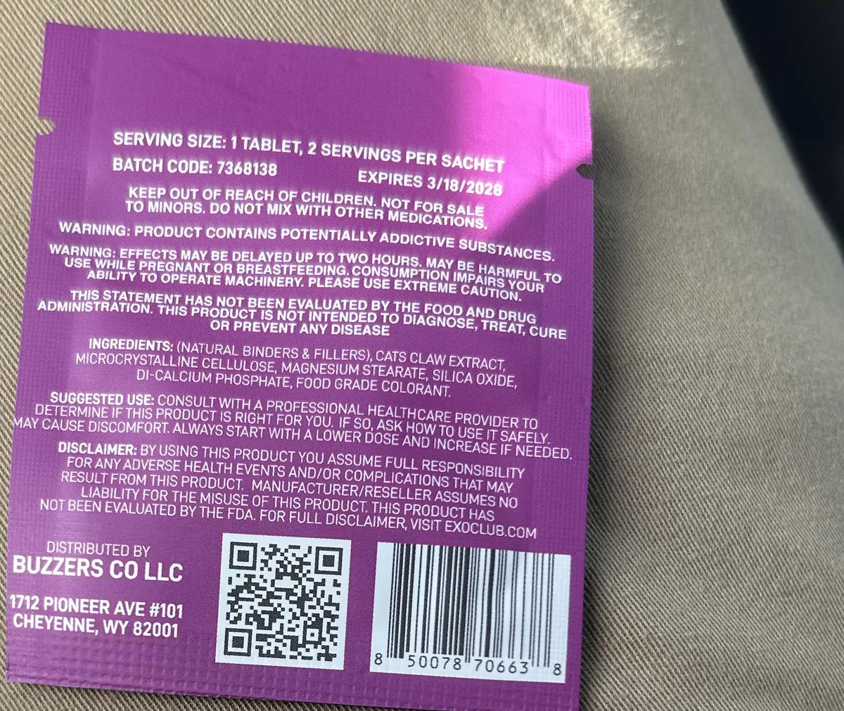 A buyer’s photo of the back of a purple Buzzers sachet: serving size, a batch code and expiry date, warnings that the product contains potentially addictive substances and is not for sale to minors, ingredients listing cats claw extract with binders, a disclaimer pointing to exoclub.com, and Distributed by Buzzers Co LLC, 1712 Pioneer Ave #101, Cheyenne, WY 82001.