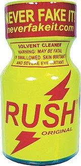 A small yellow bottle with a red Never Fake It neckband reading neverfakeit.com, a label reading Solvent Cleaner, Warning: may be fatal if swallowed, skin irritant and severe eye irritant, and the word RUSH with two red lightning bolts and ORIGINAL beneath.