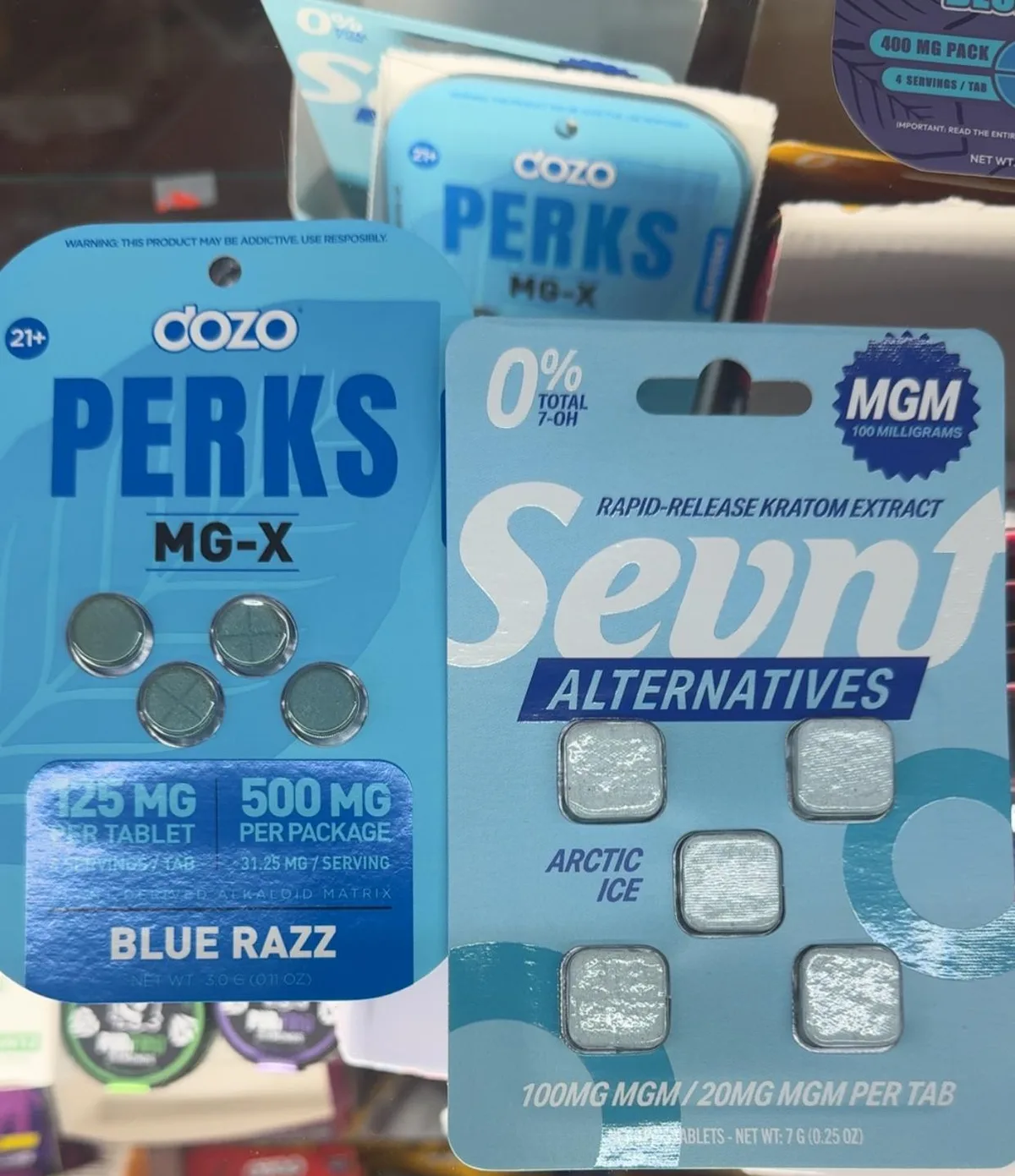 A blue Perks MG-X card on a shop counter: Warning: this product may be addictive, use responsibly; 21+; 125 mg per tablet, 500 mg per package, 31.25 mg per serving, Blue Razz. Beside it a Sevn Alternatives card reading 0% total 7-OH and MGM 100 milligrams.