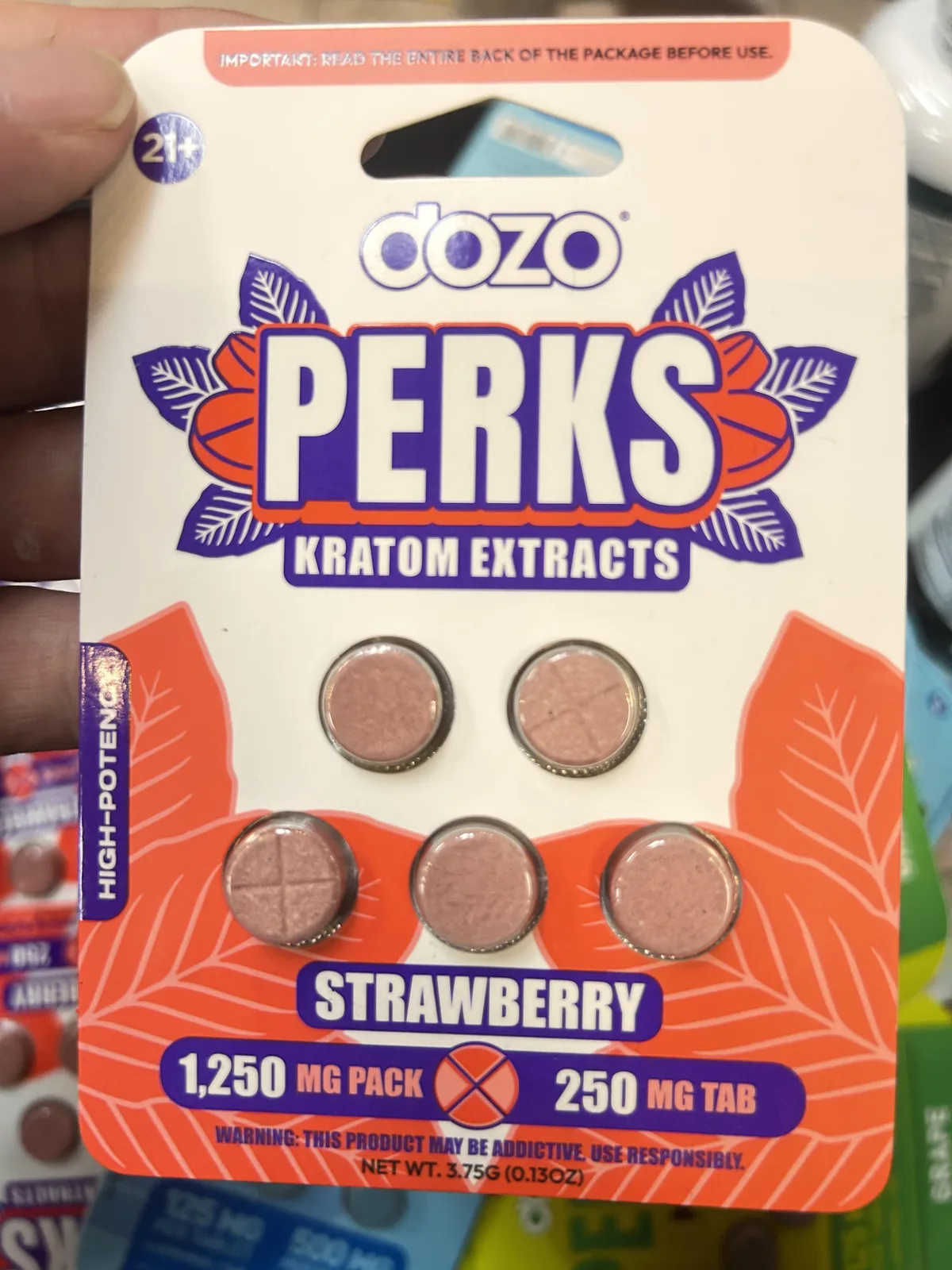 A white and orange card: dozo PERKS Kratom Extracts, high potency, Strawberry, 1,250 mg pack, 250 mg tab, Warning: this product may be addictive, use responsibly, five pink tablets.
