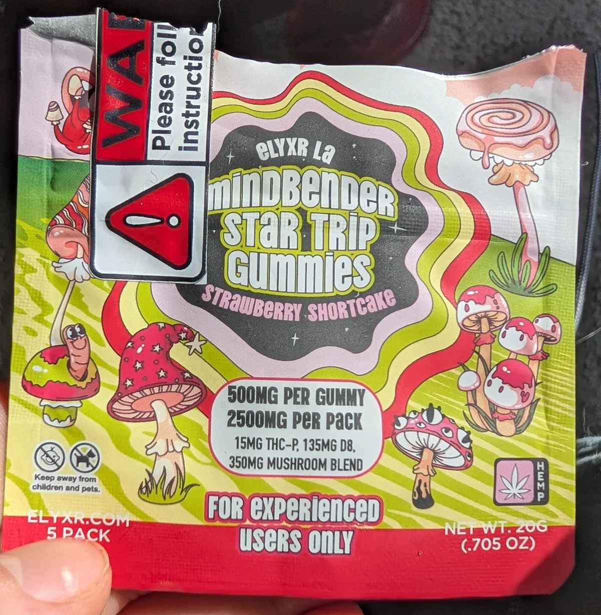 A foil pouch held in a hand: Elyxr LA Mindbender Star Trip Gummies, Strawberry Shortcake, 500mg per gummy, 2500mg per pack, 15mg THC-P, 135mg D8, 350mg mushroom blend, For experienced users only, ELYXR.COM 5 pack, a hemp leaf badge, and a warning sticker.