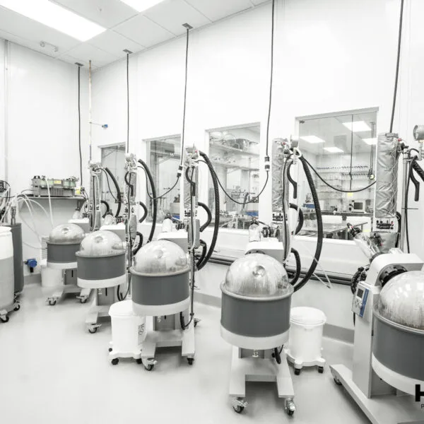A photograph published by the company of a white clean room with six large rotary evaporators with grey collection drums and glass globes, and windows into a further laboratory.
