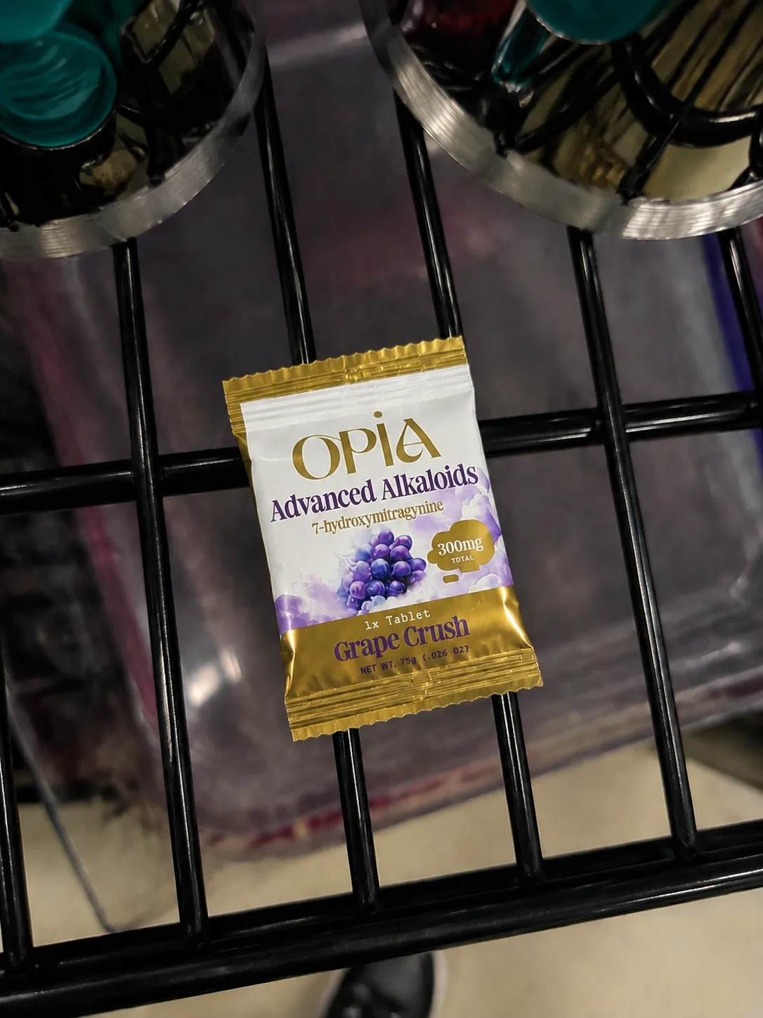 A foil packet on a wire rack: Opia Advanced Alkaloids, 7-hydroxymitragynine, 300mg total, 1x Tablet, Grape Crush.