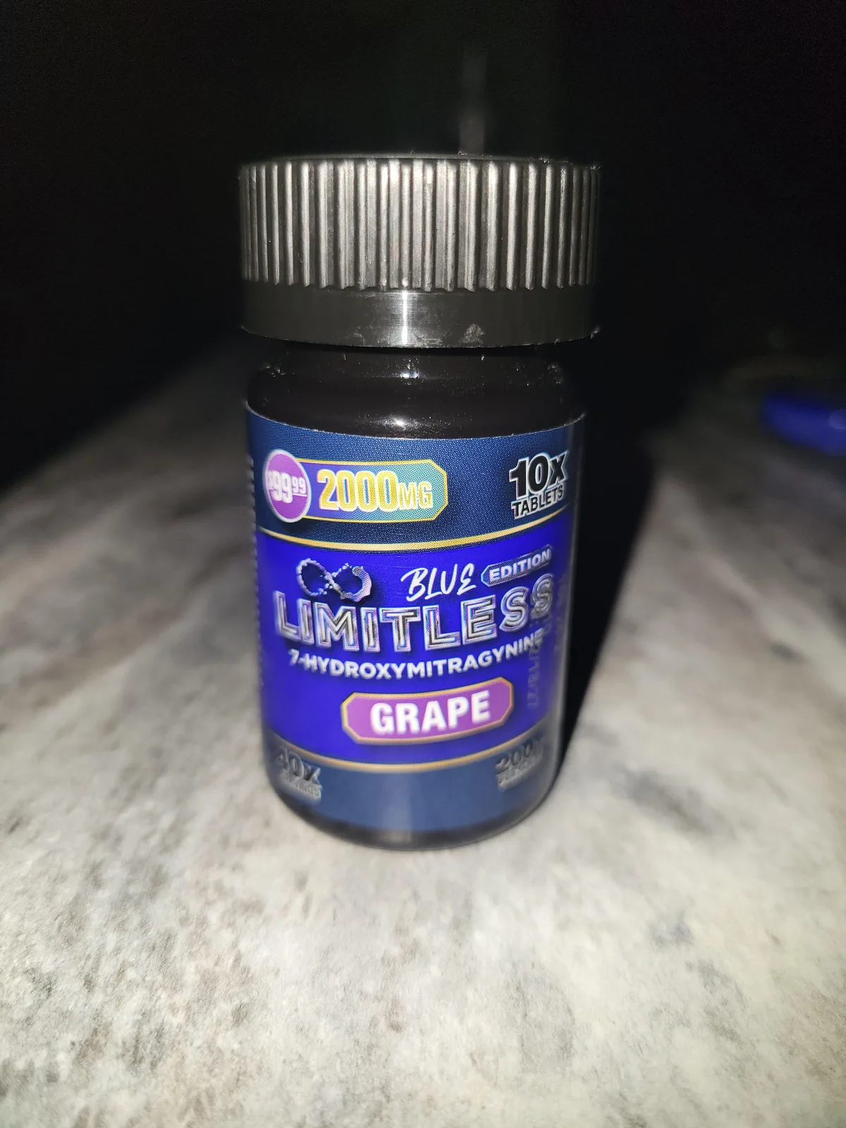 A black bottle with a blue label photographed at night: 10X tablets, 2000 MG, Blue Edition, LIMITLESS 7-HYDROXYMITRAGYNINE, Grape.