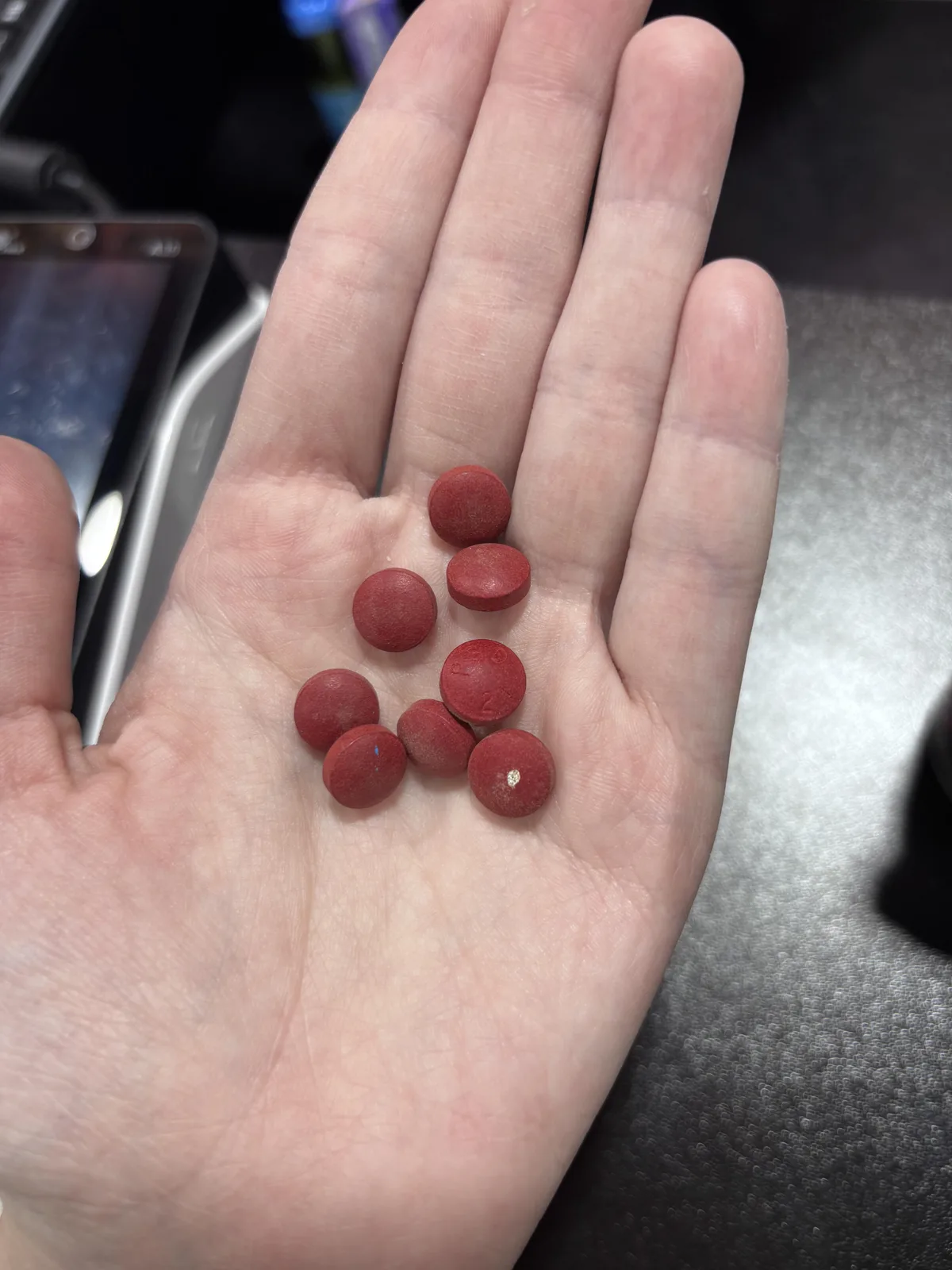 An open hand holding nine small round red tablets.