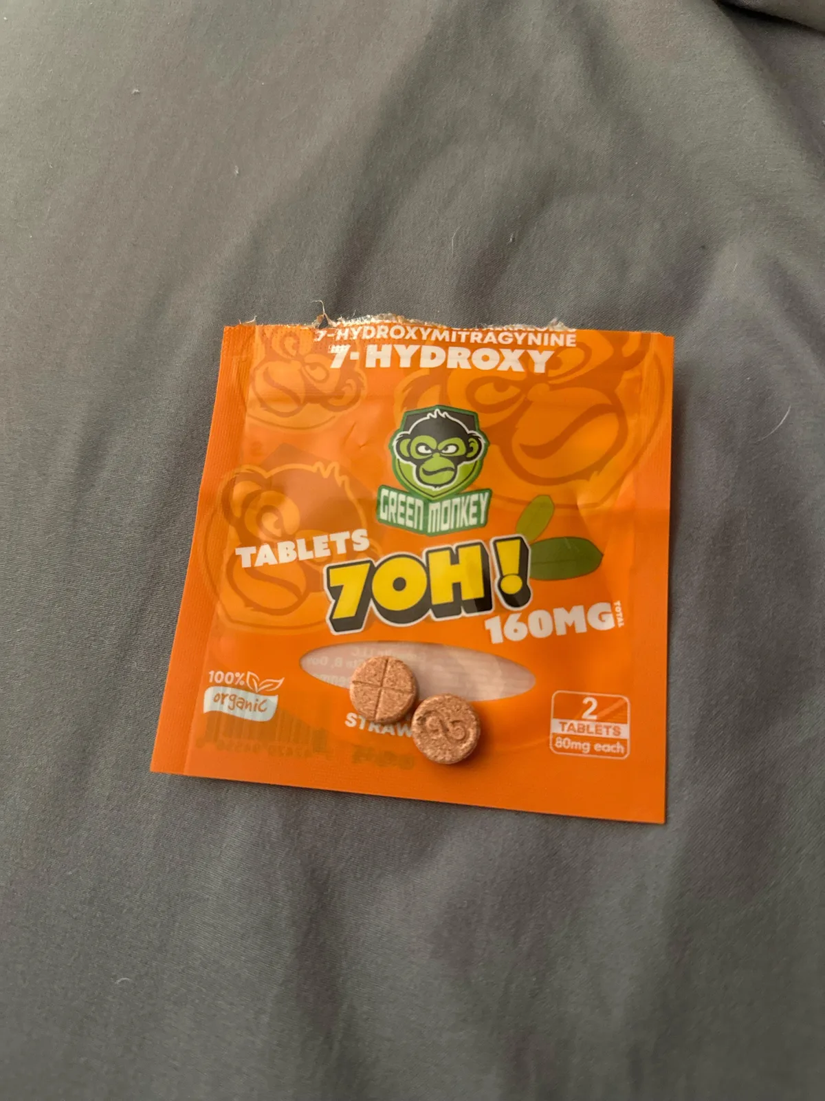 An orange foil pouch on a grey sheet: Green Monkey, 7-Hydroxy, 7OH tablets, 160 mg, two round tan tablets shown on the pouch.