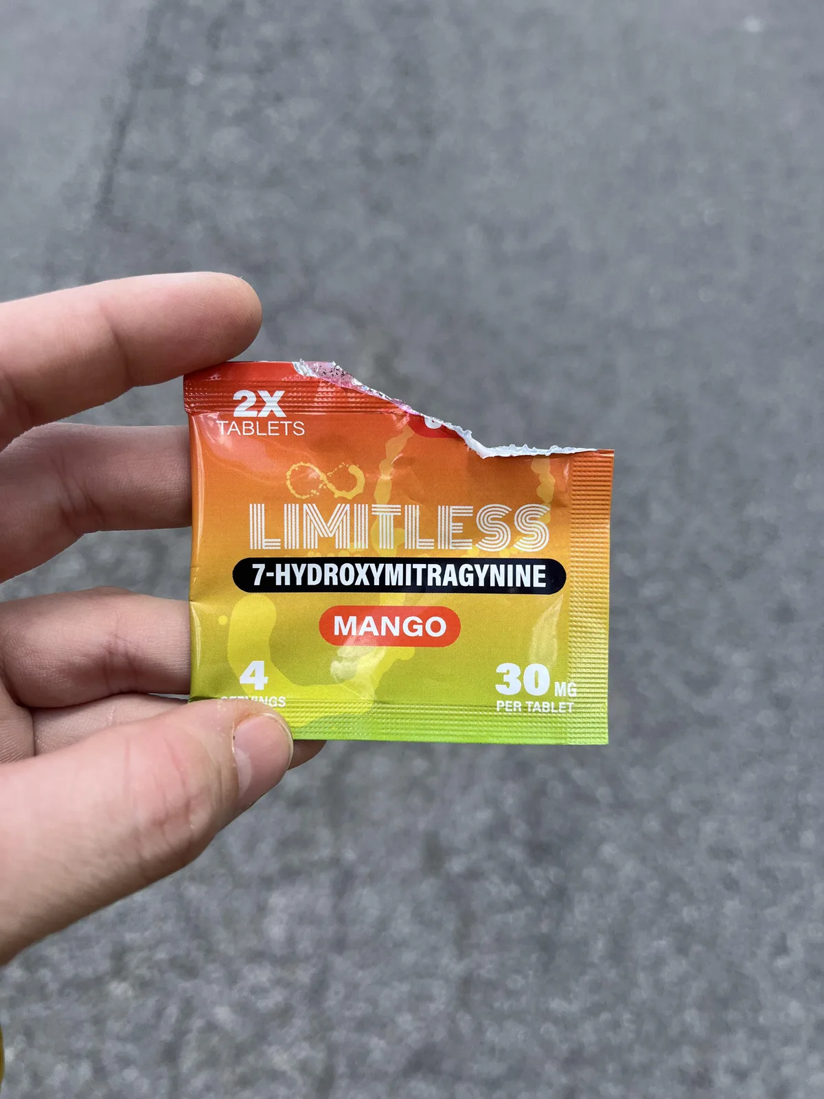 A hand holding a torn orange and green foil pouch: 2X tablets, LIMITLESS, 7-HYDROXYMITRAGYNINE, Mango, 4 servings, 30 mg per tablet.