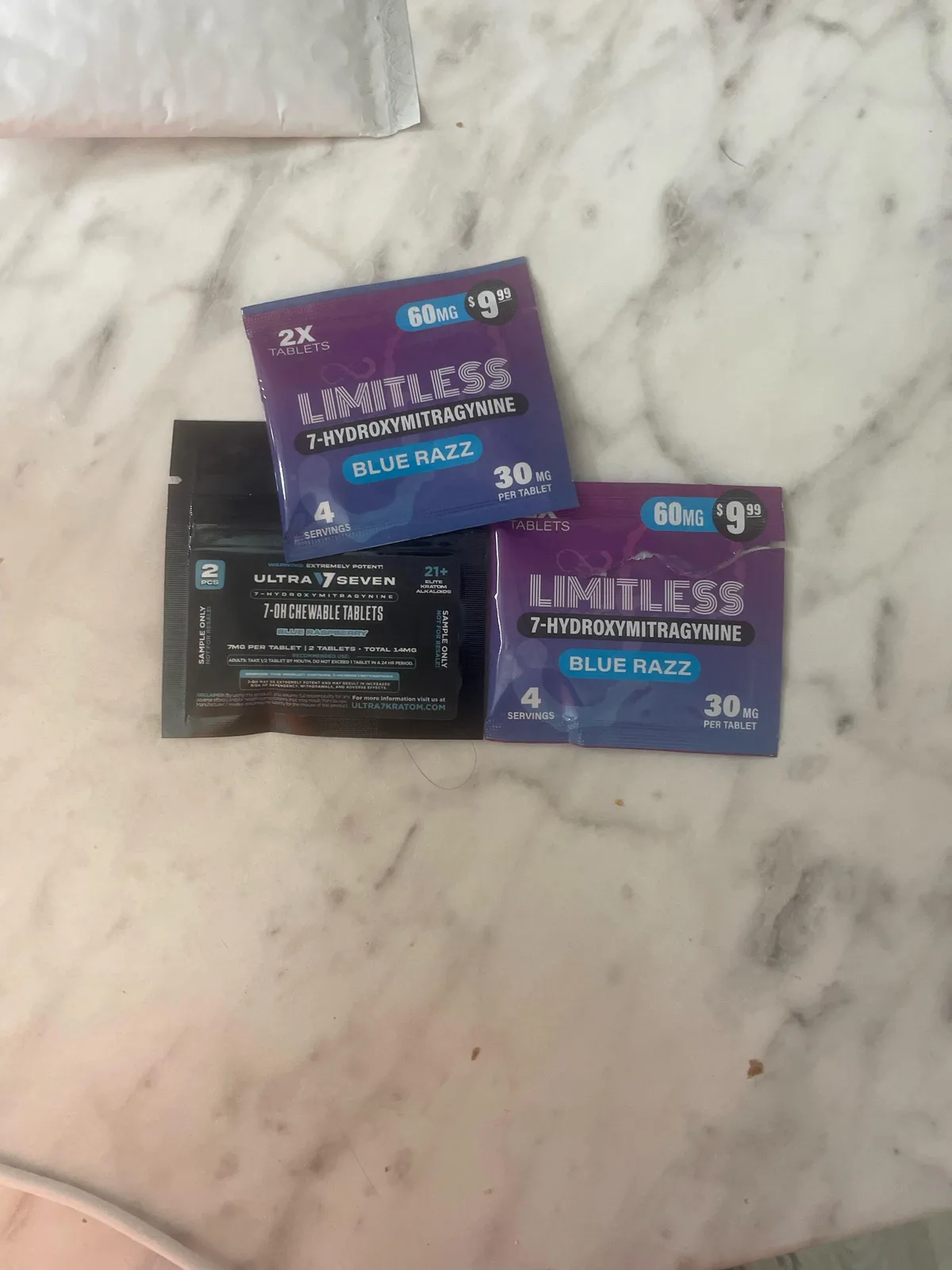 Two purple Blue Razz pouches, each printed 60 MG and 9.99 dollars, 2X tablets, 30 mg per tablet, beside a black sample pack of another brand's 7-OH chewable tablets.