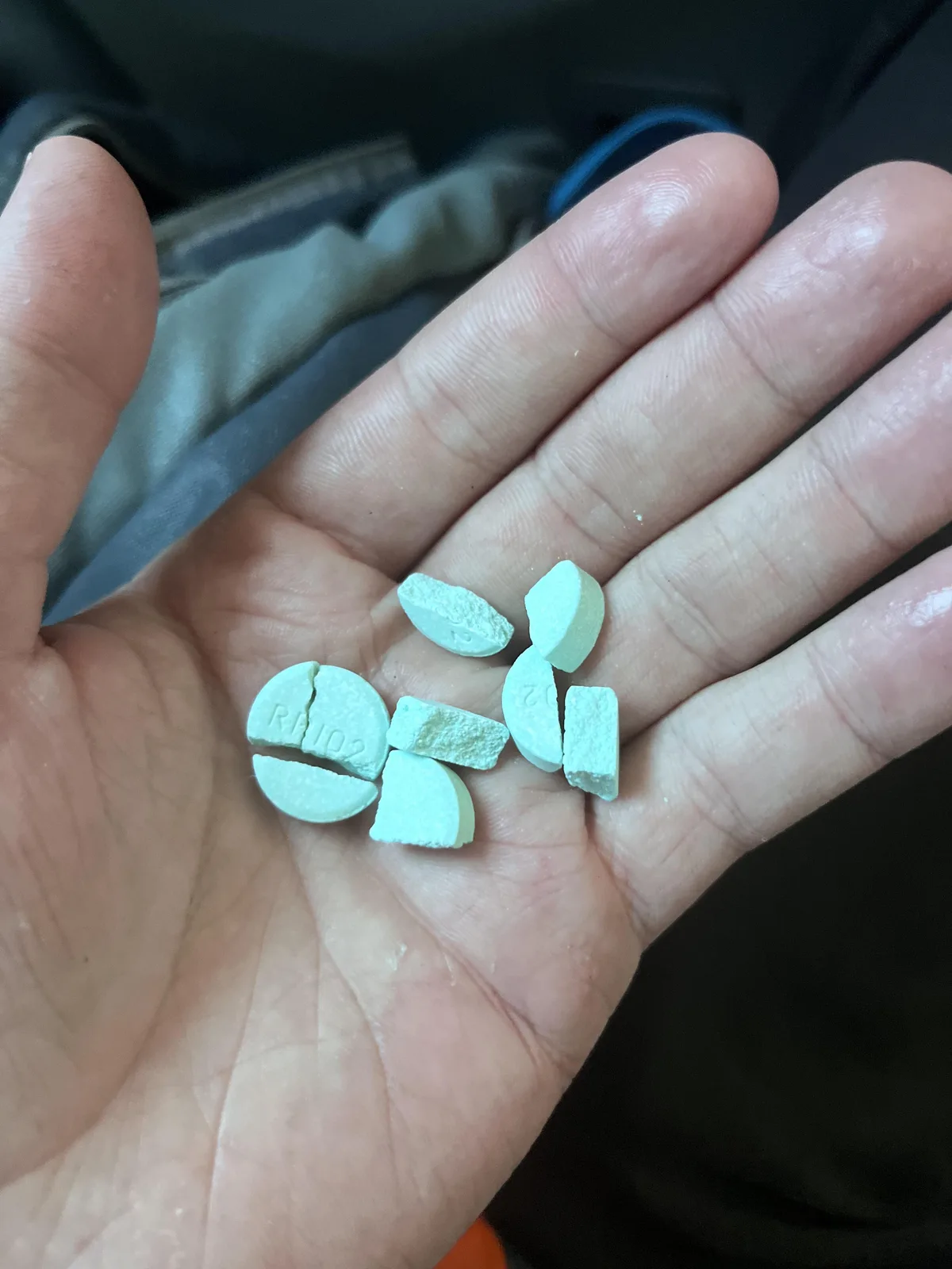 An open hand holding pale green broken tablets, some round and scored.