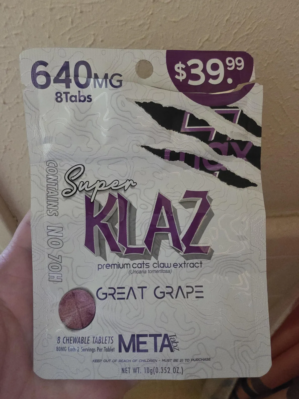 A hand holding a white Super KLAZ pouch: 640 mg, 8 tabs, premium cats claw extract (Uncaria tomentosa), Great Grape, Contains no 7OH, 8 chewable tablets, META Tabz, net weight 10 g.