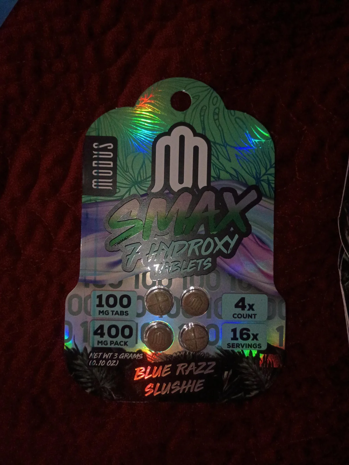 A holographic card: Modus, Smax 7 Hydroxy Tablets, 100 mg tabs, 400 mg pack, 4 count, 16 servings, net weight 3 grams, Blue Razz Slushie, with four brown tablets stamped with an M.