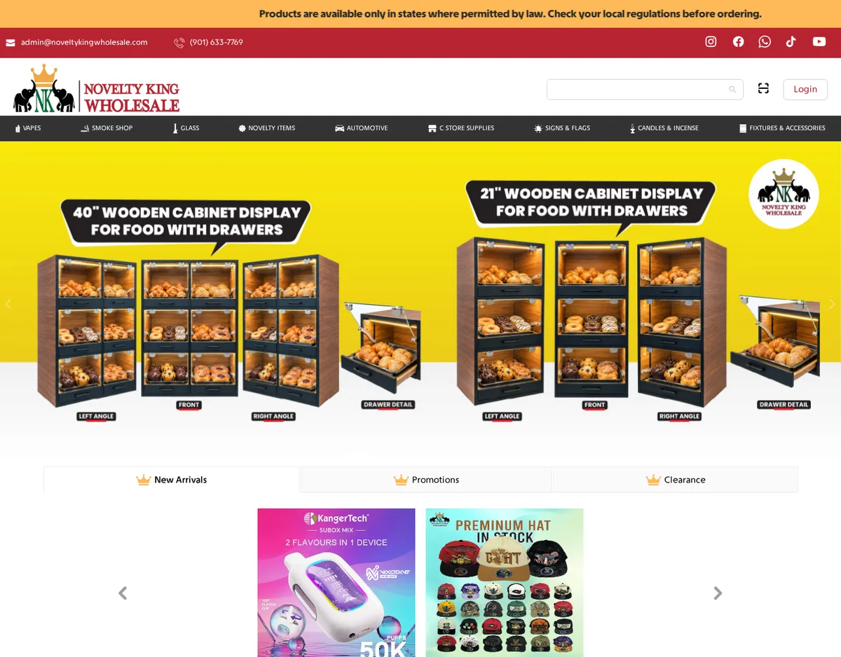 The Novelty King Wholesale home page on October 13, 2026: a top bar reading Products are available only in states where permitted by law, the company email and a 901 telephone number, a menu of vapes, smoke shop, glass, novelty items, automotive, C-store supplies, signs and flags, candles and incense, and fixtures, and a banner advertising wooden display cabinets for food.