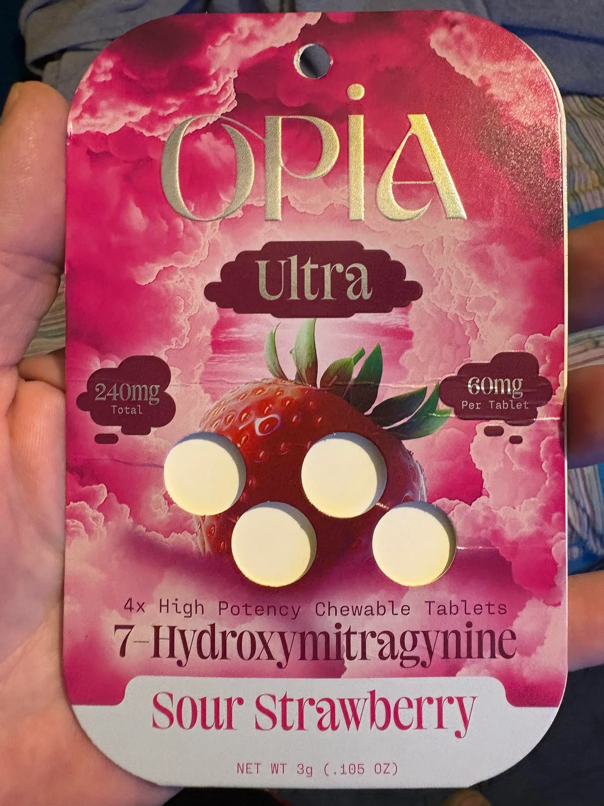 A hand holding a pink Opia Ultra card: 4x High Potency Chewable Tablets, 7-Hydroxymitragynine, Sour Strawberry, 240mg total, 60mg per tablet.