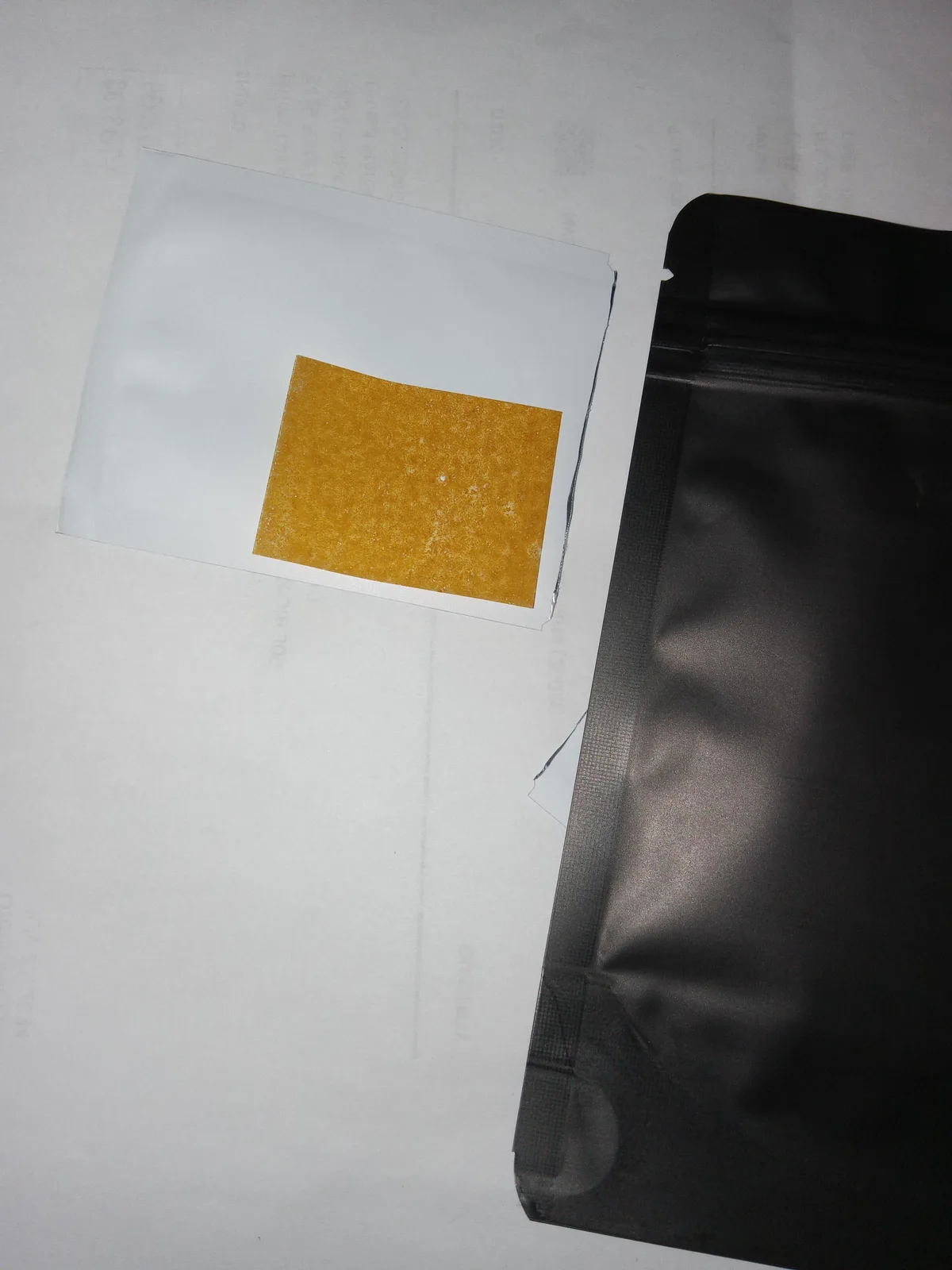 An amber strip on a plain white sachet next to a plain black zip pouch.