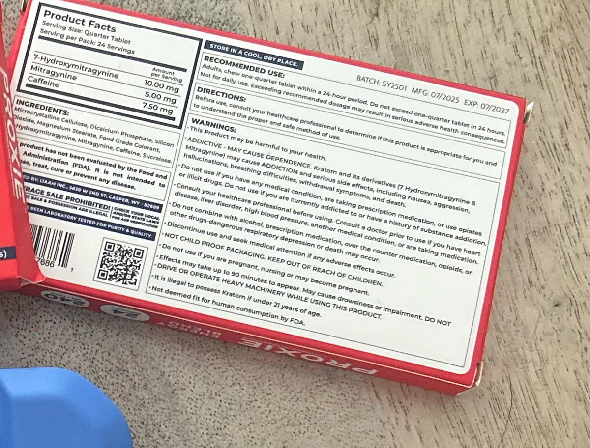 Close view of the red box's back: Product Facts per quarter tablet, 7-Hydroxymitragynine 10.00 mg, Mitragynine 5.00 mg, Caffeine 7.50 mg; batch SY2501, MFG 07/2025, EXP 07/2027; warnings including ADDICTIVE - MAY CAUSE DEPENDENCE and may cause addiction and serious side effects including death; distributed by IJAAM Inc., Casper, WY 82609; a QR code.