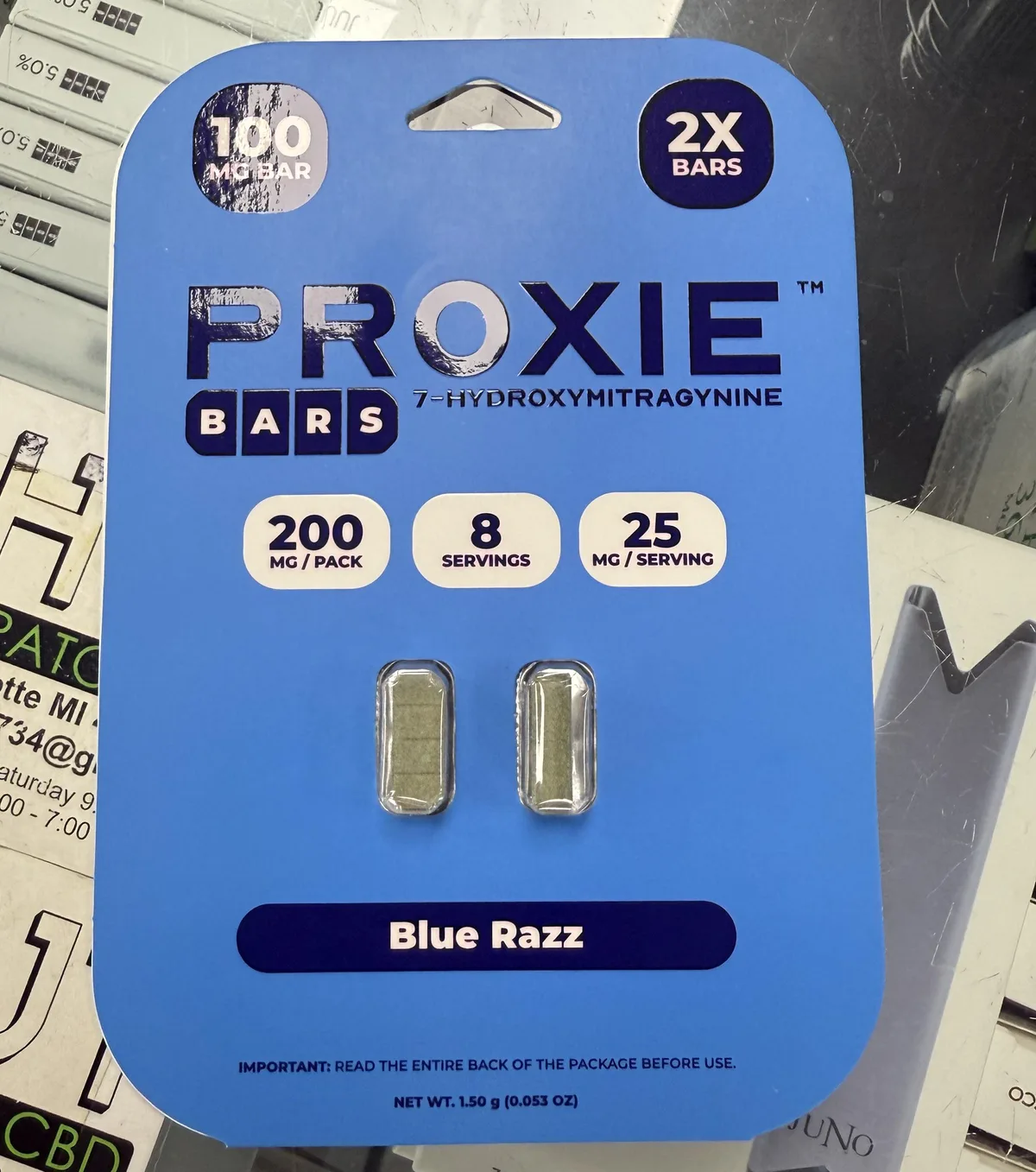A blue blister card in a shop: PROXIE BARS 7-Hydroxymitragynine, 100 MG BAR, 2X BARS, 200 mg per pack, 8 servings, 25 mg per serving, two green four-segment bar-shaped tablets, Blue Razz.