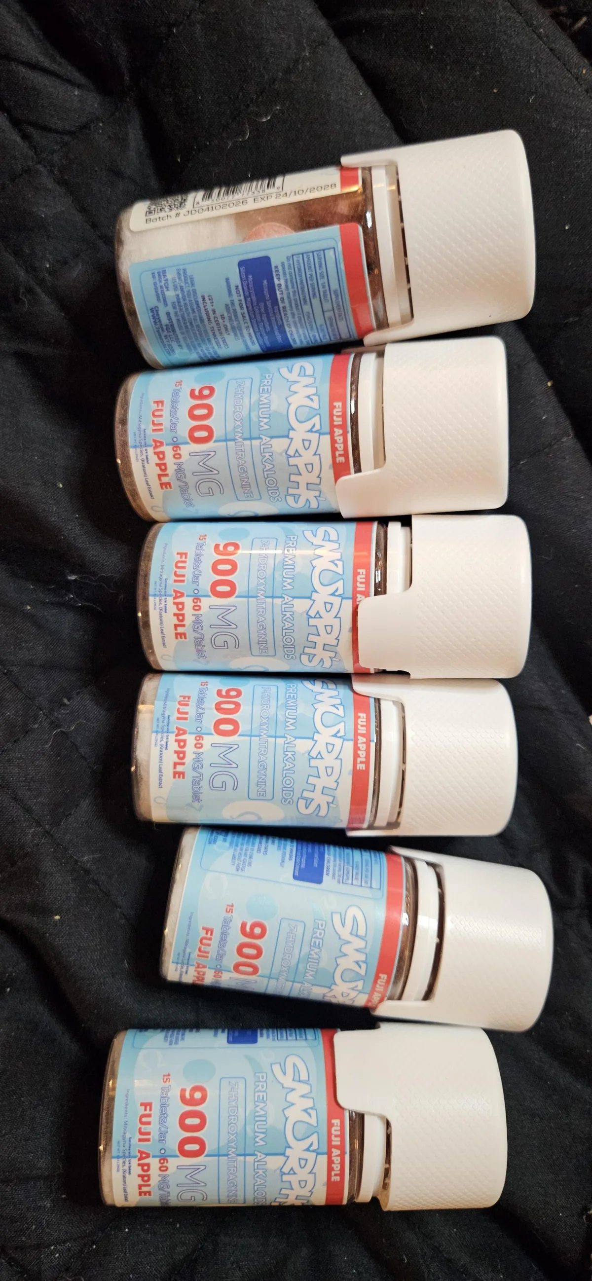 Six small bottles of Smurphs tablets, 900 MG, Fuji Apple, lying on a dark cloth, their labels set at slightly different angles.