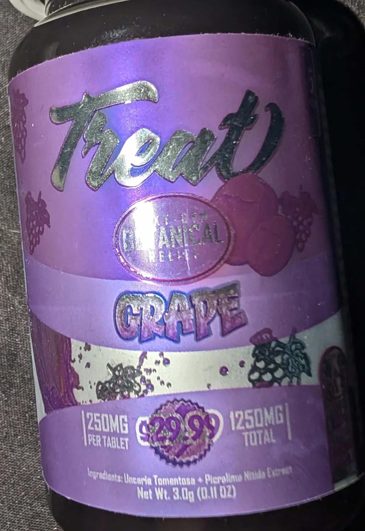 The front of a purple Treat Grape bottle: the word Treat in silver script, a round Next-Gen Botanical Relief badge, GRAPE, 250MG per tablet, 1250MG total, a shop's price sticker, and the small line Ingredients: Uncaria Tomentosa + Picralima Nitida Extract, Net Wt. 3.0g.