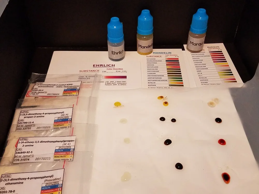 A buyer's photograph from March 2017: four small zip bags of powder with printed labels giving IUPAC names, CAS numbers and molecular weights for mebroqualone, 3C-P, 3C-E and proscaline, each dated 20170223, beside Ehrlich, Mandelin and Marquis reagent bottles, their colour charts, and drops of reagent on white paper.